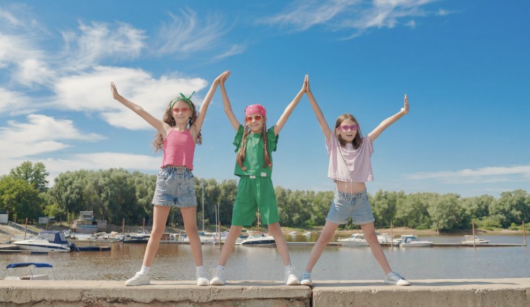 Trois enfants en tenue estivale colorée levant les bras dans une ambiance joyeuse