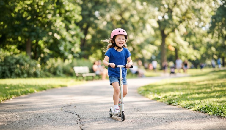 eune enfant circulant en trottinette sur une allée de parc arboré avec casque de protection