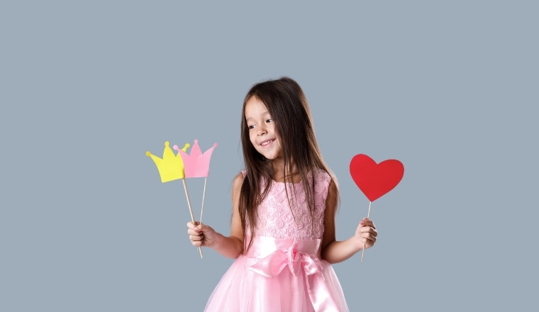 Fillette en robe rose tenant des accessoires de princesse dans un décor studio élégant