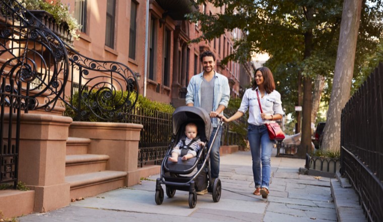 Jeunes parents promenant un bébé en poussette dans une rue résidentielle