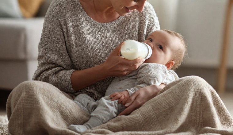 Maman donnant le biberon à son bébé assis sur ses genoux