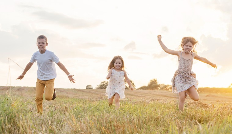 Trois enfants courant dans un champ au coucher du soleil