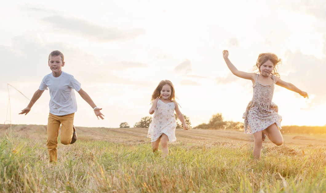 Trois enfants courant dans un champ au coucher du soleil