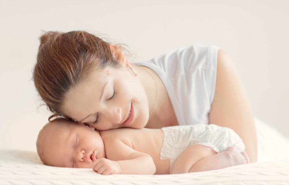 Jeune maman allongée contre son bébé endormi, moment de tendresse dans une ambiance douce et lumineuse