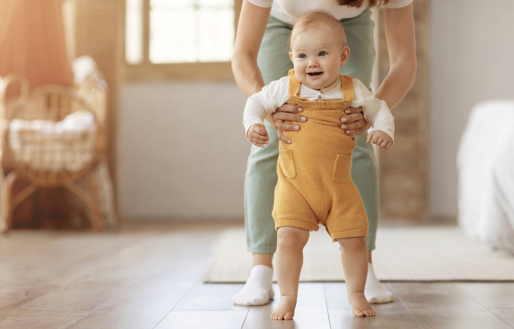 Jeune enfant faisant ses premiers pas avec l’aide de sa maman, dans une atmosphère douce et chaleureuse