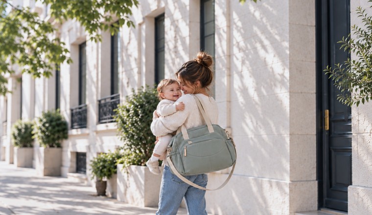 Maman portant son bébé et un sac à langer à l’épaule lors d’une promenade en ville