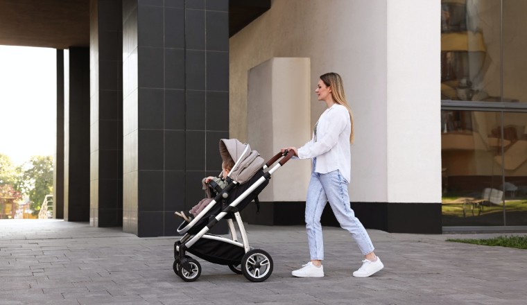 Mère promenant son enfant dans une poussette taupe devant une architecture contemporaine