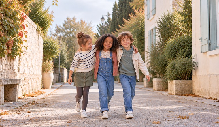Trois enfants en vêtements d'automne marchant bras dessus bras dessous dans une rue